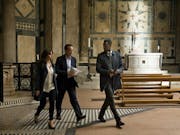 A white woman, white woman and Black man in suits walking with purpose through an ornate church