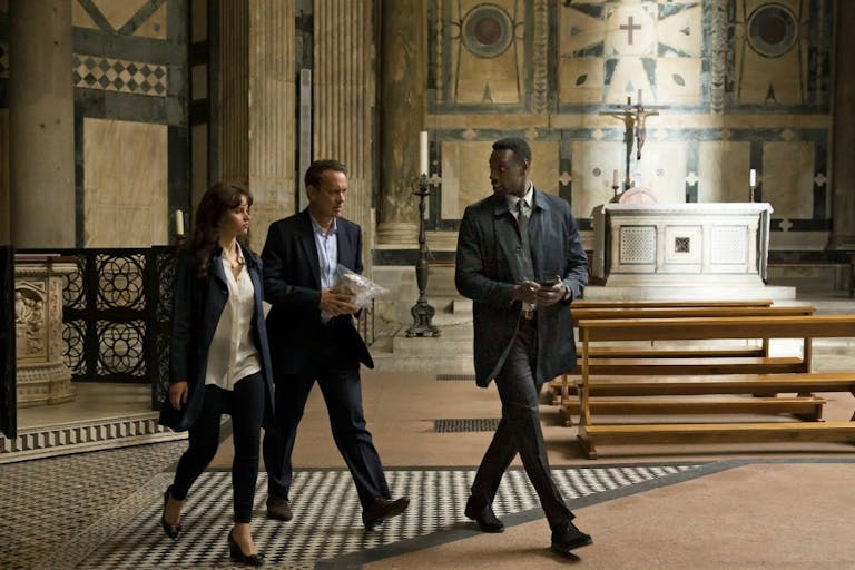 A white woman, white woman and Black man in suits walking with purpose through an ornate church