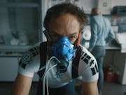A white man in a blue fitness oxygen mask in cycling clothes riding a bike in a lab setting, looking strained