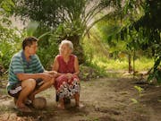 A young Indonesian man sits with an old Indonesian woman in a lush green forest