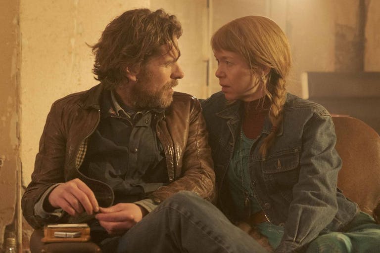 A white man with scruffy beard and a white woman with long ginger hair in a plait sitting on a sofa looking intently at each other