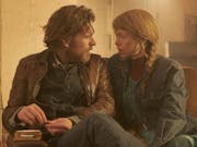 A white man with scruffy beard and a white woman with long ginger hair in a plait sitting on a sofa looking intently at each other