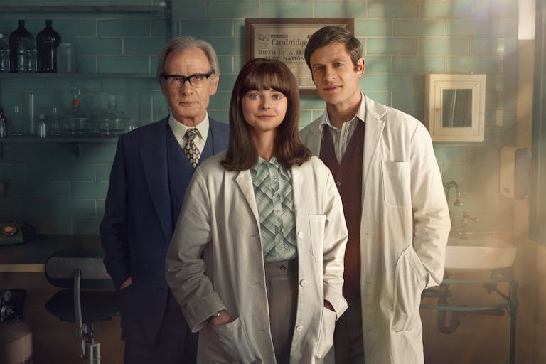 A middle aged white man in a blue suit and a young white woman and man in white lab coats