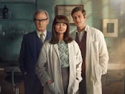 A middle aged white man in a blue suit and a young white woman and man in white lab coats