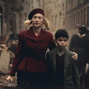 A young white woman walking down a war torn street in 1940s with her arm around a young mixed race Black boy