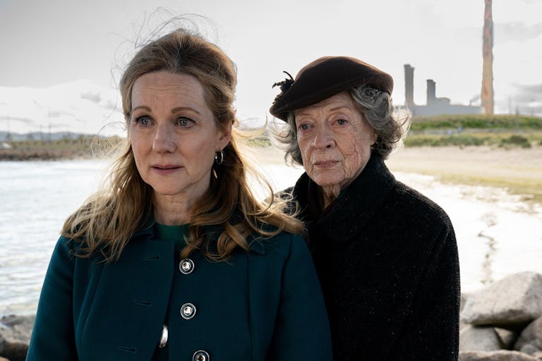 One middle aged woman and one old woman stand next to each other on a beach shore