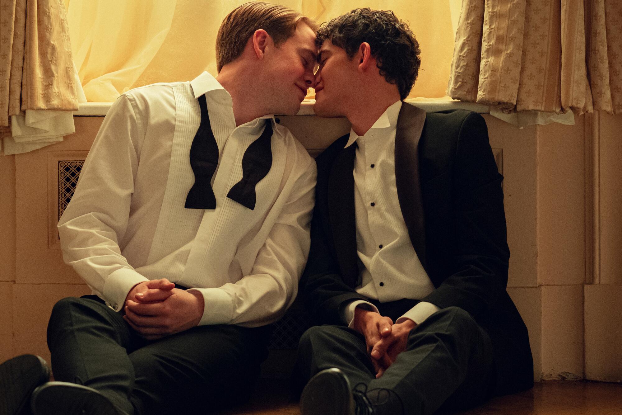 Two young white boys in dressy attire, sitting on a bedroom floor about to kiss
