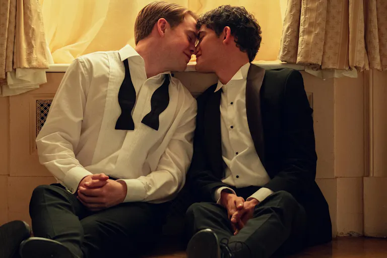 Two young white boys in dressy attire, sitting on a bedroom floor about to kiss