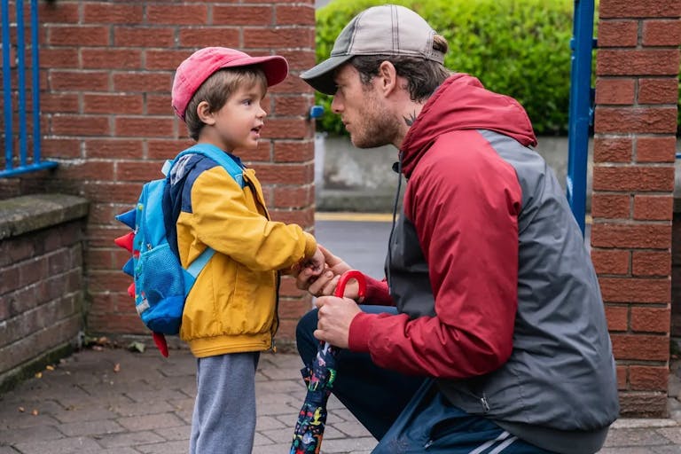 Man kneels down to talk to a young boy in a yellow jacket.
