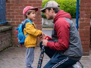 Man kneels down to talk to a young boy in a yellow jacket.
