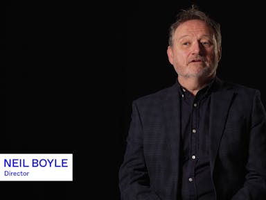 A middle aged white man in a dark suit and shirt, on screen name tag reads 'Neil Boyle, Director'