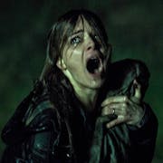 A white woman wet through, flattened dark wet hair, holding a bundle tighten, screaming and looking frightened