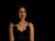 A young brown woman with short dark hair, red lipstick and black dress smiles at the camera