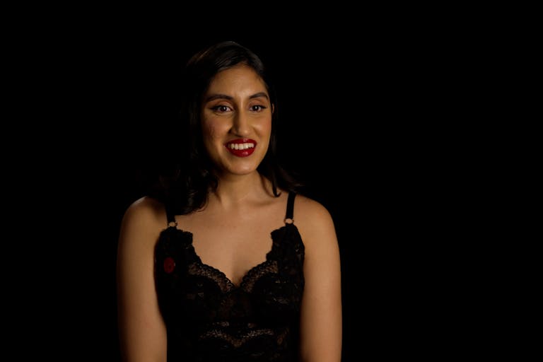 A young brown woman with short dark hair, red lipstick and black dress smiles at the camera