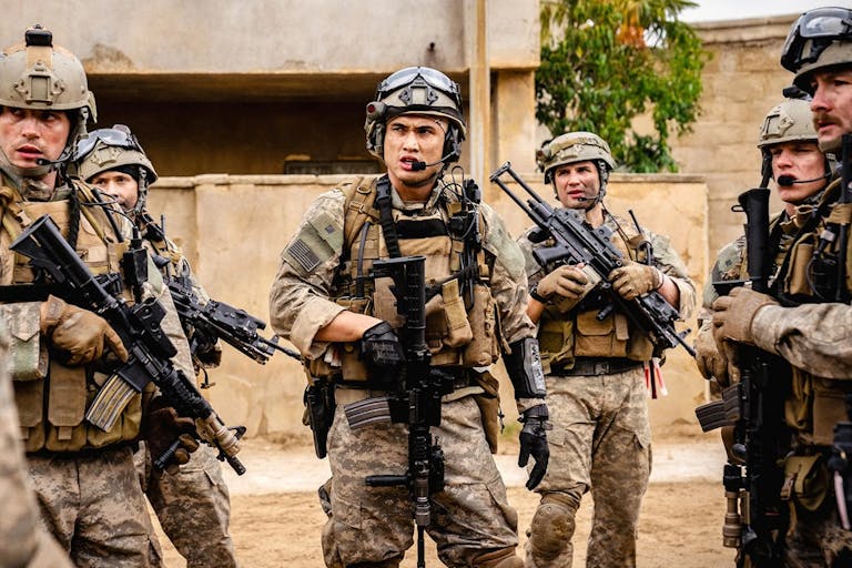A group of young men in Iraq wearing US army uniform helmets and holding rifles loosely