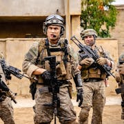 A group of young men in Iraq wearing US army uniform helmets and holding rifles loosely