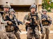A group of young men in Iraq wearing US army uniform helmets and holding rifles loosely