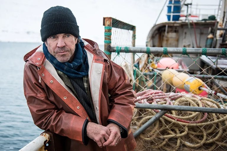 A white middle aged man in a thick waterproof coat, jumper and beanie hat, on a small fishing vessel