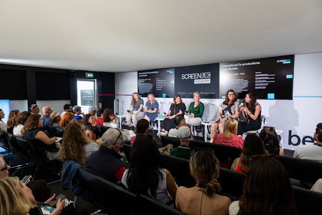 an audience watches a panel of six female speakers