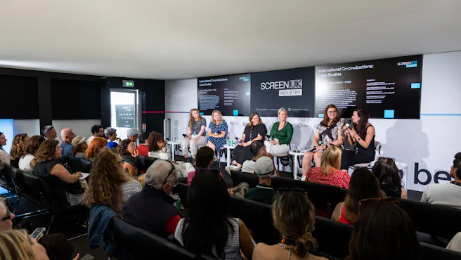 an audience watches a panel of six female speakers