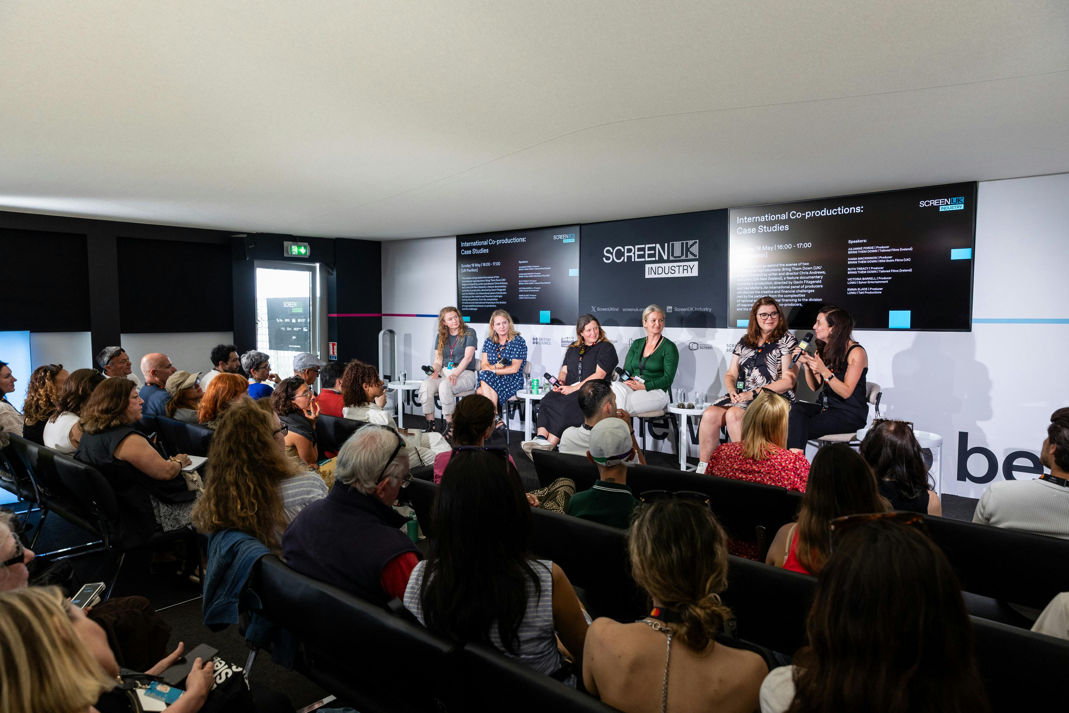 an audience watches a panel of six female speakers