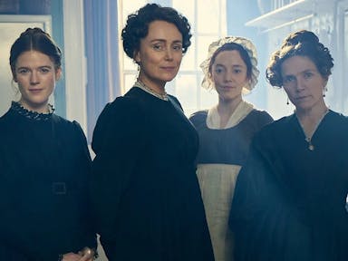 Four white woman in period clothes with their hair pulled up