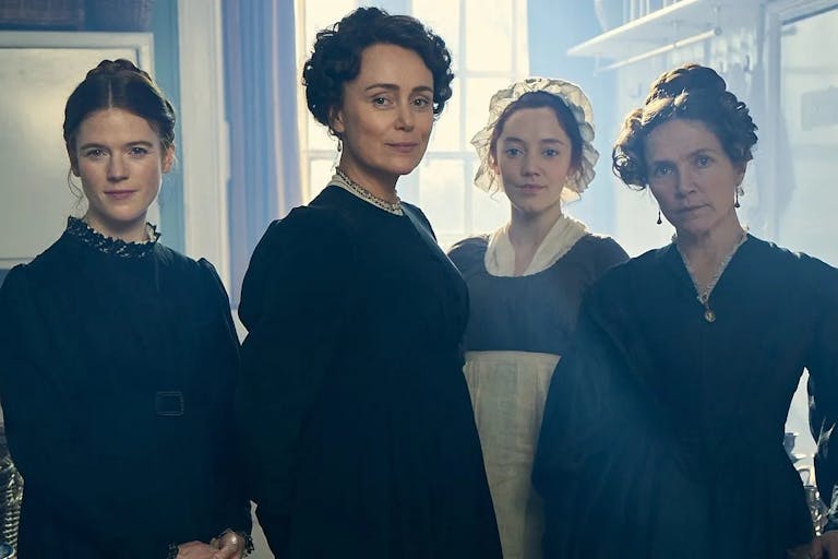 Four white woman in period clothes with their hair pulled up
