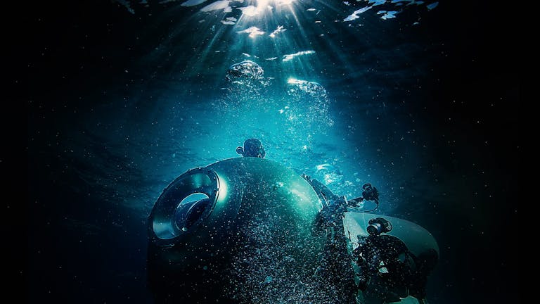 A small commercial submarine in the dark, gloomy ocean with a strip of blue light illuminating it from above