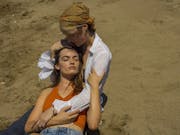 A young white woman nestled in another older white woman's arms as they lounge on the beach