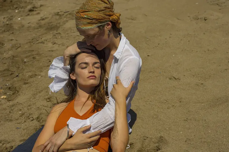 A young white woman nestled in another older white woman's arms as they lounge on the beach