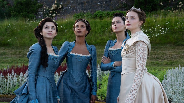 Four young women, three in blue elegant regency dresses and one in an ivory wedding dress