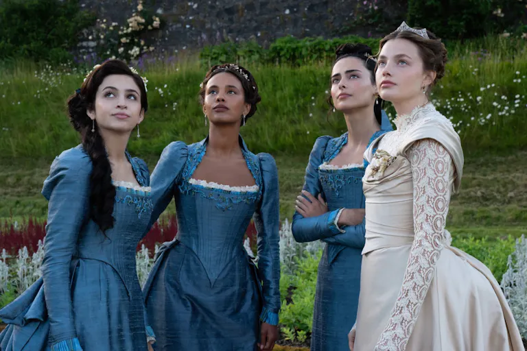 Four young women, three in blue elegant regency dresses and one in an ivory wedding dress