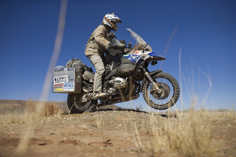 A man in motorbike clothing and helmet, riding on a motorbike through a hot, dry landscape