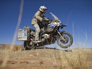 A man in motorbike clothing and helmet, riding on a motorbike through a hot, dry landscape