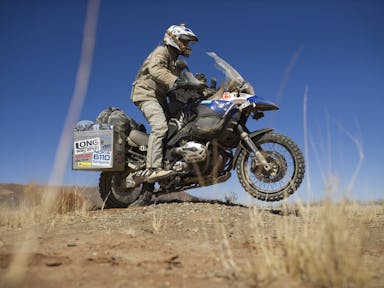 A man in motorbike clothing and helmet, riding on a motorbike through a hot, dry landscape