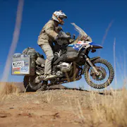 A man in motorbike clothing and helmet, riding on a motorbike through a hot, dry landscape