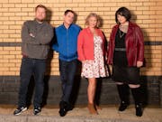 forur white people, two men and two women standing in front of a brick wall facing the camera