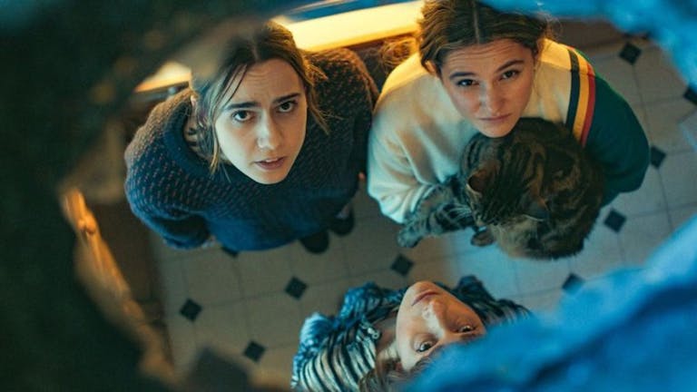 Three young white women, one holding a cat, looking a hole in the ceiling