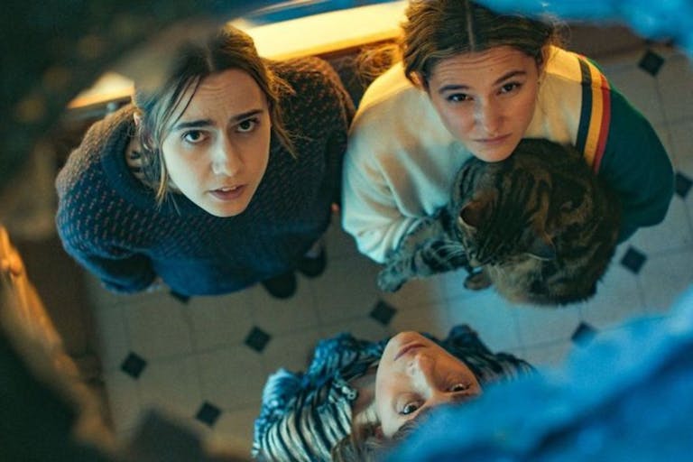 Three young white women, one holding a cat, looking a hole in the ceiling