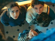 Three young white women, one holding a cat, looking a hole in the ceiling