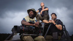 A Black man and two white men sit on an offroad jeep in explorer clothing holding a large camera