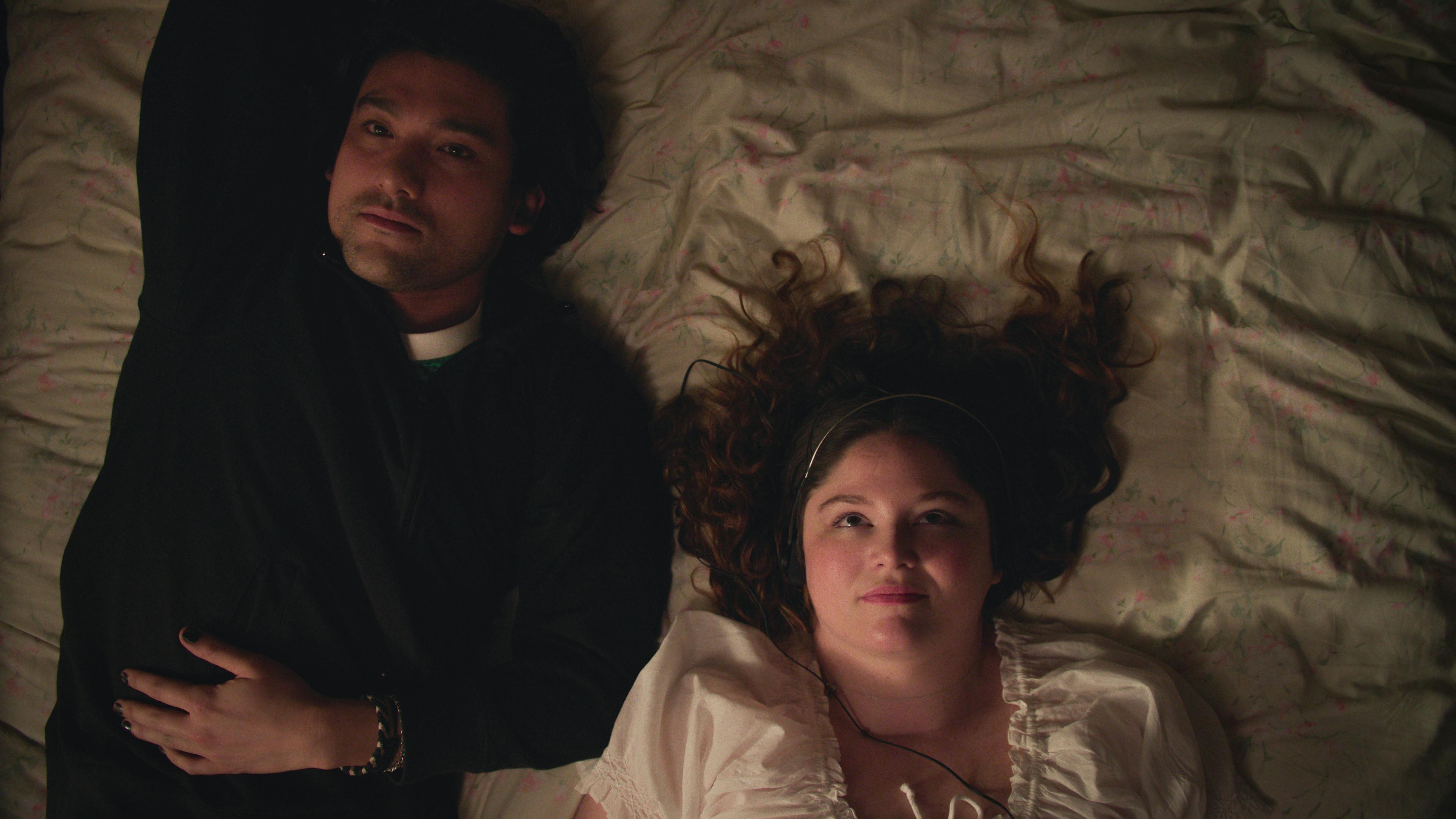 A British-Japanese young man and a white young woman lay on a bed looking up at the ceiling