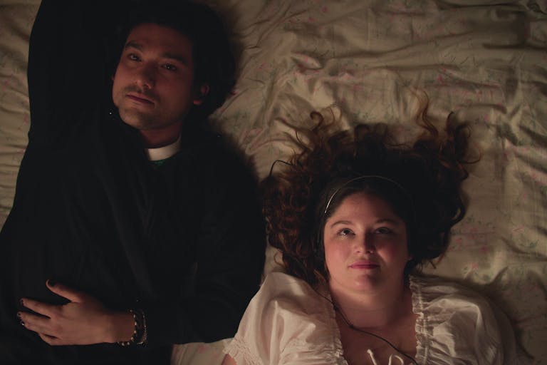 A British-Japanese young man and a white young woman lay on a bed looking up at the ceiling