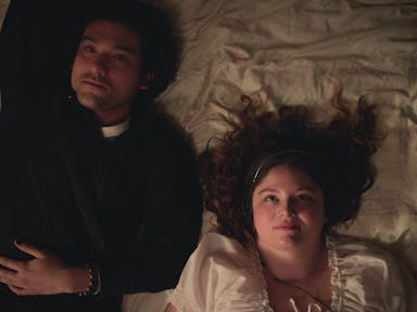 A British-Japanese young man and a white young woman lay on a bed looking up at the ceiling