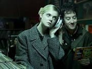 A blonde girl and a dark haired boy, listening to music near a collection of vinyl records