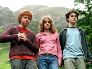 A ginger white teen boy holding a rat stands next to a white teen girl and a white teen boy wearing glasses with a scar on his forehead