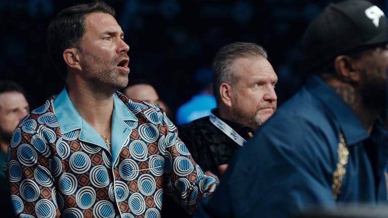 A white man in a colourful shirt in a crowd with other men shouting enthusiastically 