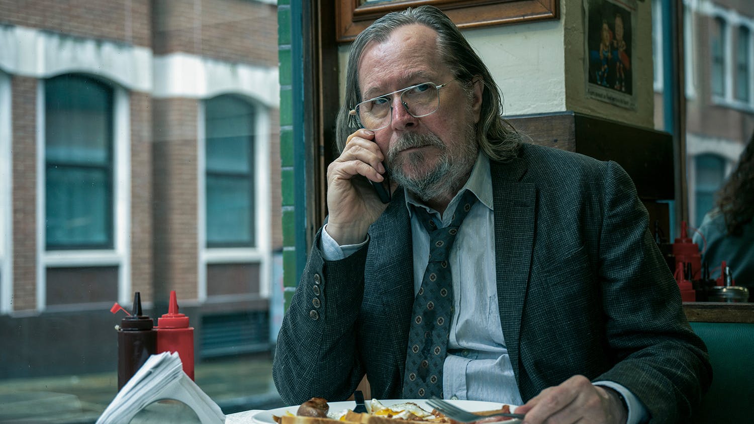 A bedraggled middle aged white man in a tired suit eating a fry up at a greasy spoon café while on the phone