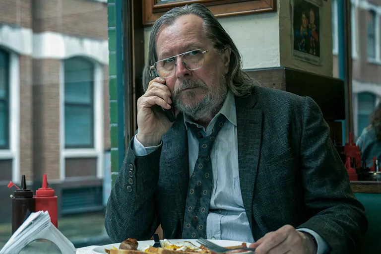 A suited white middle-aged man with shoulder length hair, on the phone in a cafe