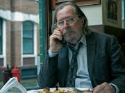 A bedraggled middle aged white man in a tired suit eating a fry up at a greasy spoon café while on the phone